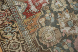 Distressed vintage Malayer rug close-up: brick red border, muted teal and ivory field, visible knot heads.