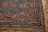 Distressed antique Soumac carpet with madder red field, zig-zag border, wave motif, and fringe.