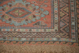 Distressed madder red Soumac carpet corner with geometric zig-zag, wave borders, and fringe.