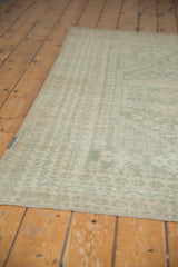 Distressed Oushak rug corner showing faded seafoam green and ivory geometric motifs.