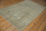 Distressed vintage Oushak rug corner, revealing worn seafoam green and beige geometric patterns.