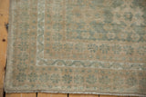 Distressed Oushak rug corner showing even wear, muted seafoam green, beige tones, and fringe.