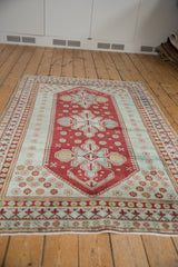 Caucasian rug's cherry red, seafoam geometric border, floral patterns, and worn pile.