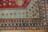 Distressed vintage Caucasian rug with seafoam floral field and cherry red geometric pawn motif border.