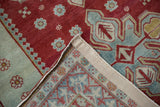 Distressed cherry red and seafoam Caucasian rug, folded to show its intricate hand-knotted reverse.