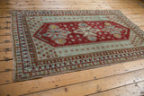 Distressed vintage Caucasian rug corner, showing cherry red floral field, seafoam border, and geometric motifs.