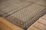 Textured corner of distressed Oushak carpet with speckled sand and chocolate brown patterns.