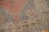 Distressed Oushak rug corner, dusty blush field, worn pale slate gray and ivory borders.