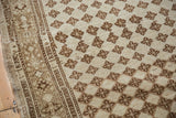 Distressed ivory field with brown floral diamonds and detailed geometric border.