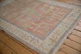 Corner of distressed vintage Oushak rug with blush, ivory, blue vinery and fringe.