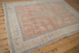 Distressed Oushak rug corner, blush field with primitive patterns, ivory border, and fringe.