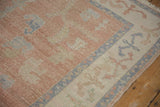 Distressed blush and ivory field with vinery motif and dusty blue patterned border on vintage Oushak.