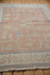 Distressed Oushak corner: blush field, dusty blue vinery border, and ivory fringe.