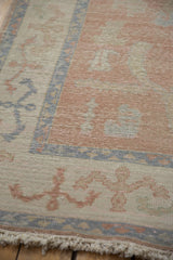 Distressed Oushak rug close-up: blush, ivory, dusty blue vinery, worn pile, and fringe.