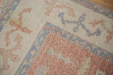 Distressed vintage Oushak carpet with blush vinery, dusty blue border, and worn pile texture.