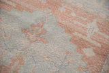 Distressed Oushak carpet close-up, showing worn knot heads, blush, and pale blue geometric motifs.