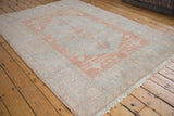 Blush and pale blue distressed Oushak rug corner, showing worn pile and ivory fringe.