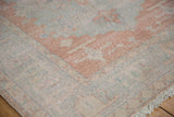 Distressed Vintage Oushak carpet corner with worn blush, pale blue, ivory geometric patterns and fringe.