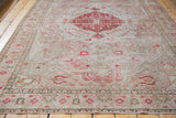 Angled view of distressed Oushak rug, showcasing faded blush floral patterns and woven texture.