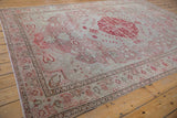 Corner view of distressed Oushak carpet with pale blush floral border and visible textured wear.