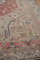 Angled view of a distressed Oushak rug showing its low pile and geometric motifs in blush and beige.