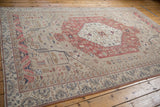 Angled view of a vintage distressed Oushak carpet with a blush hexagonal medallion and beige field.