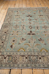 Angled view down the length of a distressed Hamadan rug with soft seafoam and brown tones.