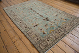 Angled view of a distressed Hamadan rug with large-scale palmettes in seafoam and brown.