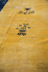 Textured saffron field of a Peking rug with a clear indigo pictorial potted plant motif.