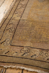 Distressed vintage Khotan carpet corner with charcoal scrolling clouds border and worn saffron yellow pile.