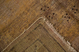 Distressed Khotan carpet corner revealing hand-knotted back, fringed edge, and worn saffron yellow pile.