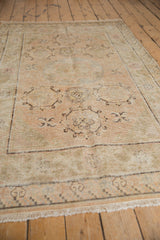 Distressed texture of a vintage Khotan rug, showing visible wear, fringe, and infinity knot motifs.