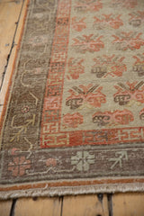 Distressed Khotan rug corner, revealing germinating plant motifs, pale orange border, and worn fringe.