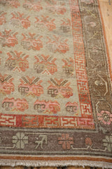 Distressed Khotan rug corner showing pale orange geometric border and germinating plant motifs.