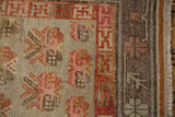 Distressed vintage Khotan rug corner, revealing foundation wear, beige field, faded plant motifs, and geometric border.