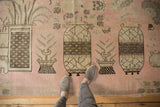 Pictorial landscape design of stylized vases and plants on a distressed pink Khotan rug.