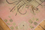 Pictorial stylized foliage in pink and sand tones on the corner of a distressed Khotan rug.