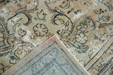 Distressed Arak rug corner shows worn ivory floral motifs and woven blue foundation.