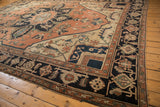 Geometric floral cross-sections on antique Serapi carpet field of pale terracotta, cream, and navy.