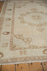Distressed coffee brown germinating plant motifs across the vintage Oushak rug's ivory field.