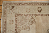 Distressed Oushak rug showing abrashed antique ivory field and worn brown border.