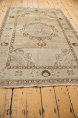 Corner of distressed vintage Oushak rug, antique ivory field with coffee brown botanical patterns.