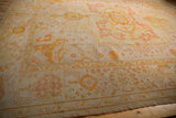 Antique Oushak rug's wide banded border with pale lemon, saffron, and blush curvilinear patterns.
