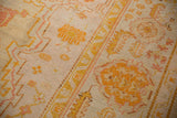 Antique Oushak's splayed floral and dragon-inspired arabesques in saffron and blush with even wear.