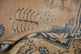 Folded vintage Khotan rug detail: distressed pale bronze field, dark tree motifs, navy border.