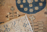 Folded vintage distressed Khotan rug corner, showing back weave, fringe, and worn ivory floral guls.