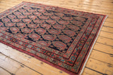Intricate red, blue, and green border patterns on a vintage Senneh rug's navy boteh field.