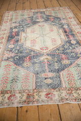 Detail of distressed vintage Sparta rug texture showing dark blue, mint green, and pale cherry motifs with wear.