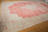 Angled view of a distressed Oushak carpet showing its faded cherry red field and wide ivory border.