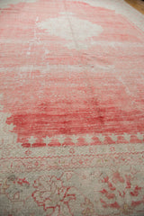 Textural wear across the faded cherry red and ivory pile of a distressed vintage Oushak carpet.